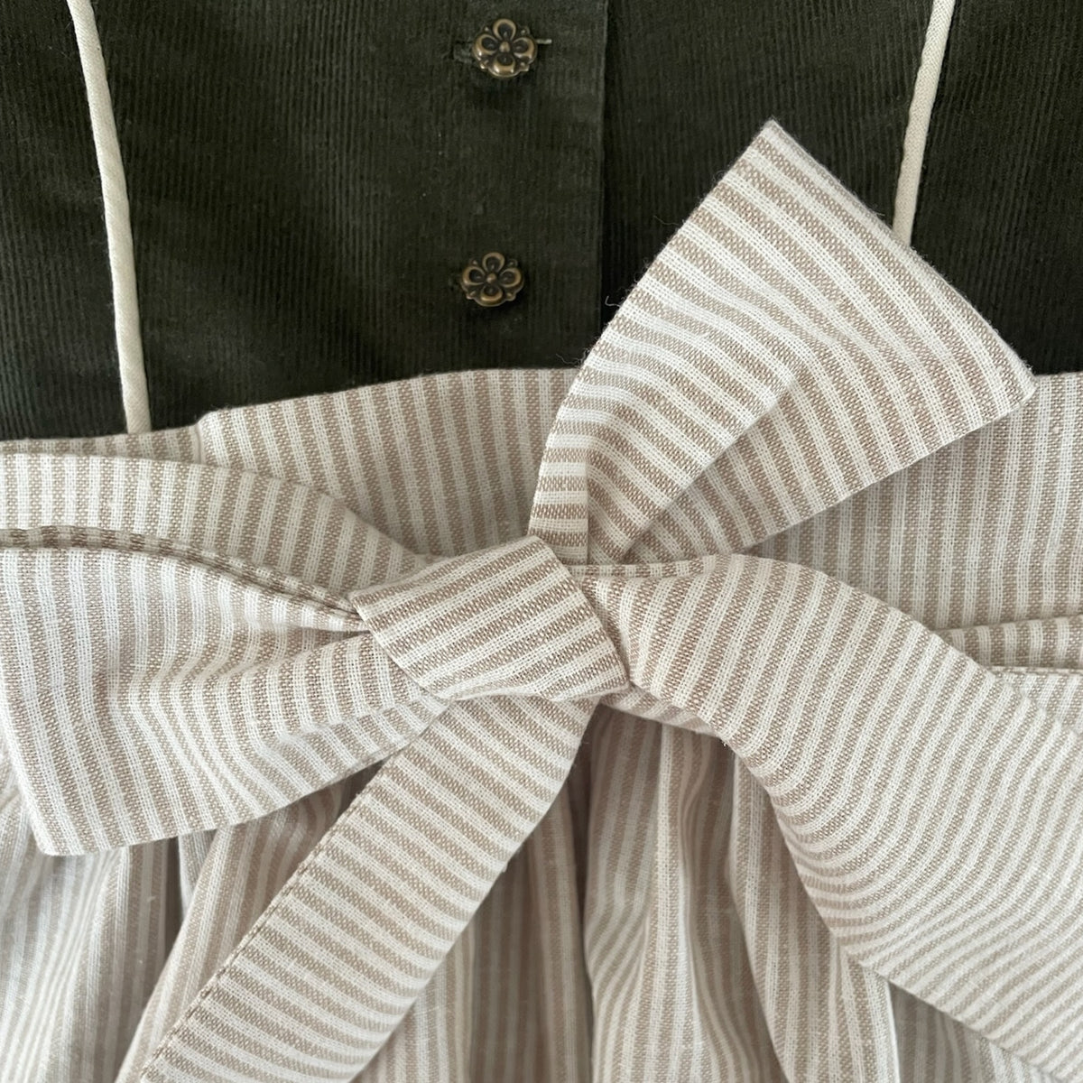 Detail des dunkelgrünen Oberteils und der gebundenen Schürze von Dirndl Grete