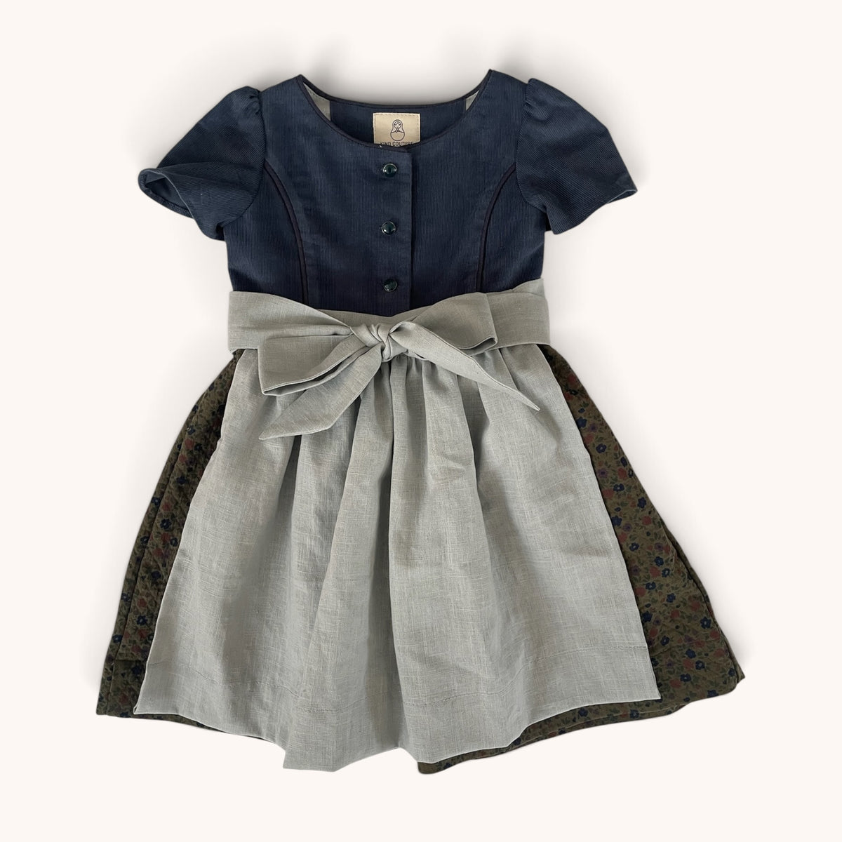 Dirndl Ottilie mit tiefblauem Oberteil, gemustertem Rock und hellgrauer Leinenschürze