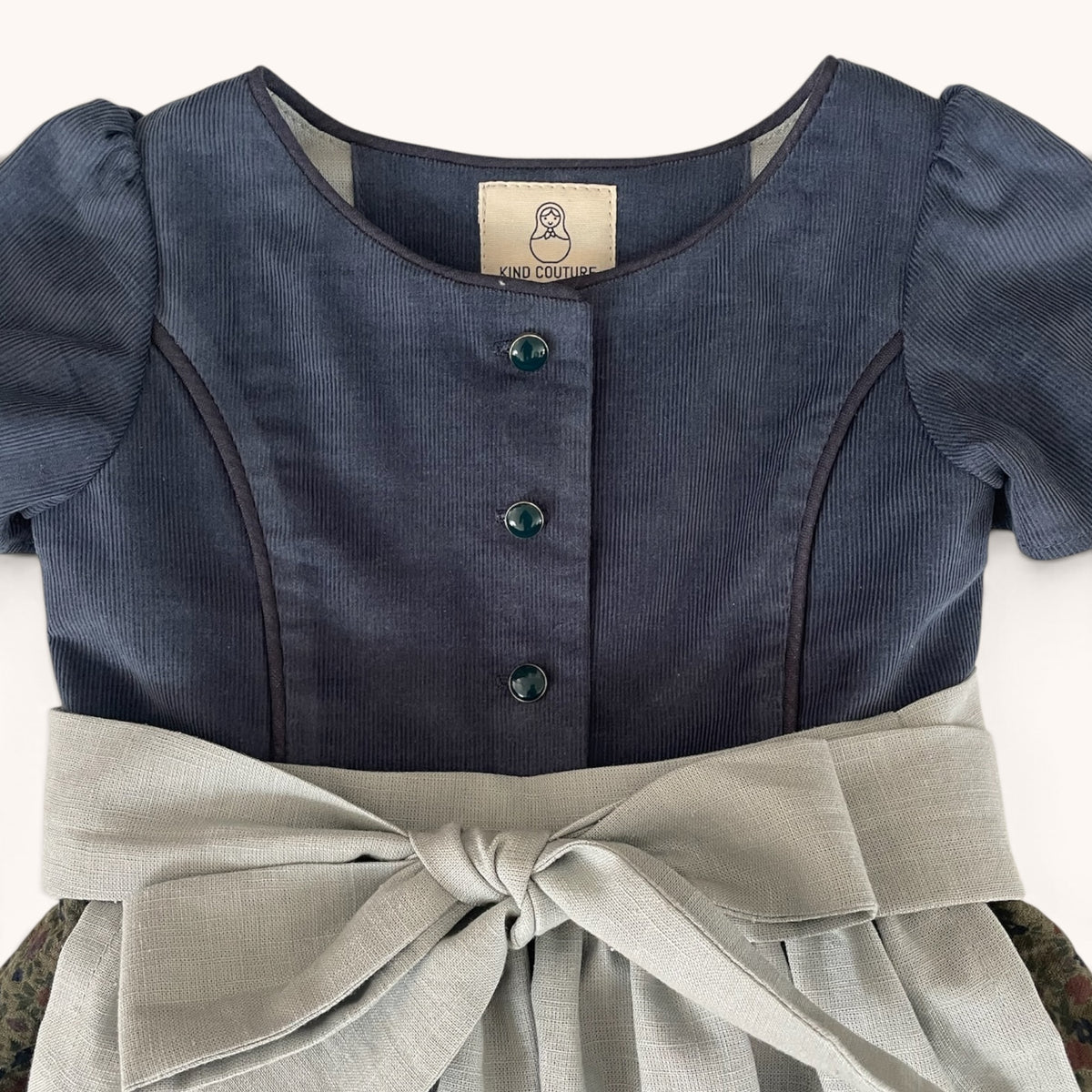 Tiefblaues Oberteil, gemusterter Rock und hellgraue Leinenschürze von Dirndl Ottilie
